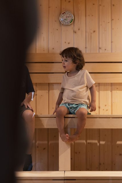 Criança sentada num banco de madeira da sauna